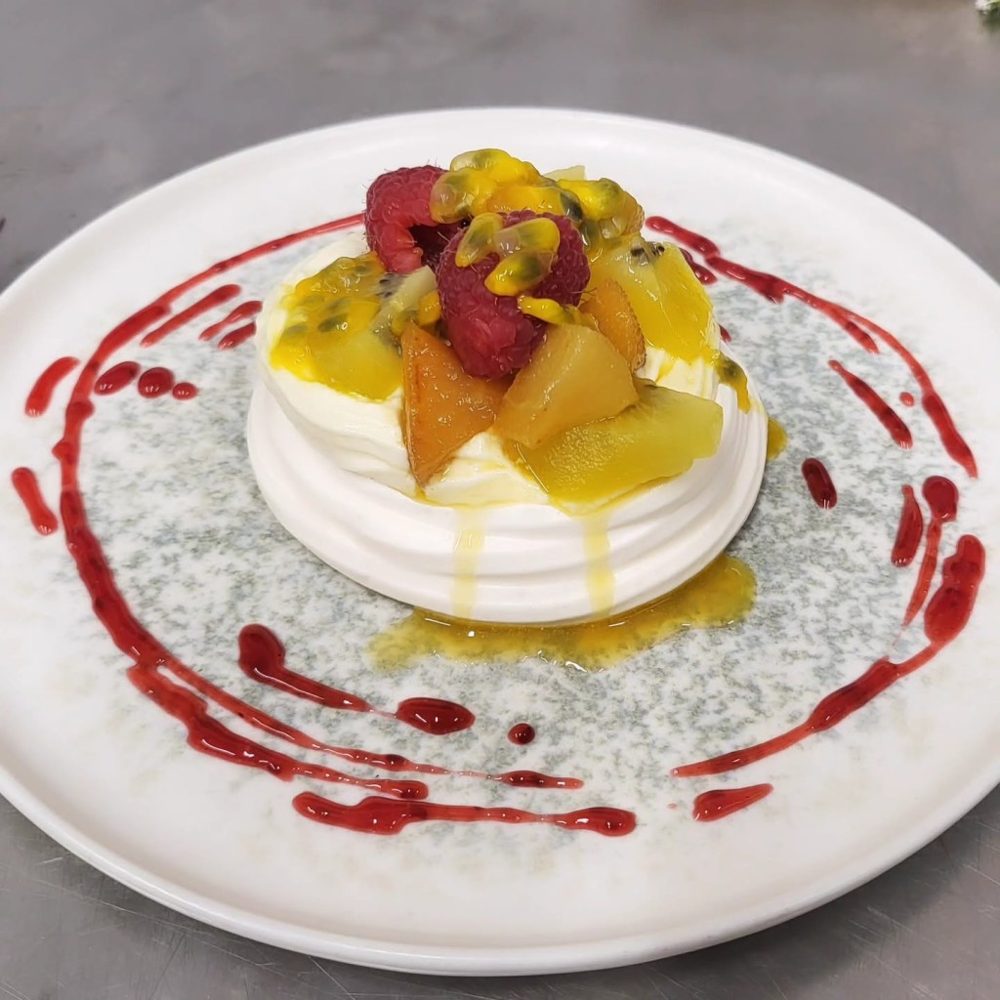 Une pavlova garnie de fruits jaunes et d'un coulis rouge