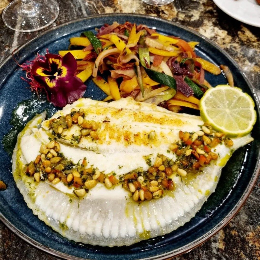 Un filet de poisson sur une crème, parsemé de pistaches, avec des légumes et du citron vert