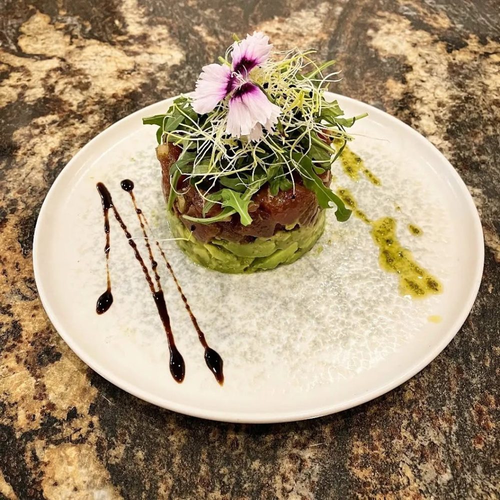 Un tartare surmonté de graines germées et d'une fleur, sur une assiette blanche